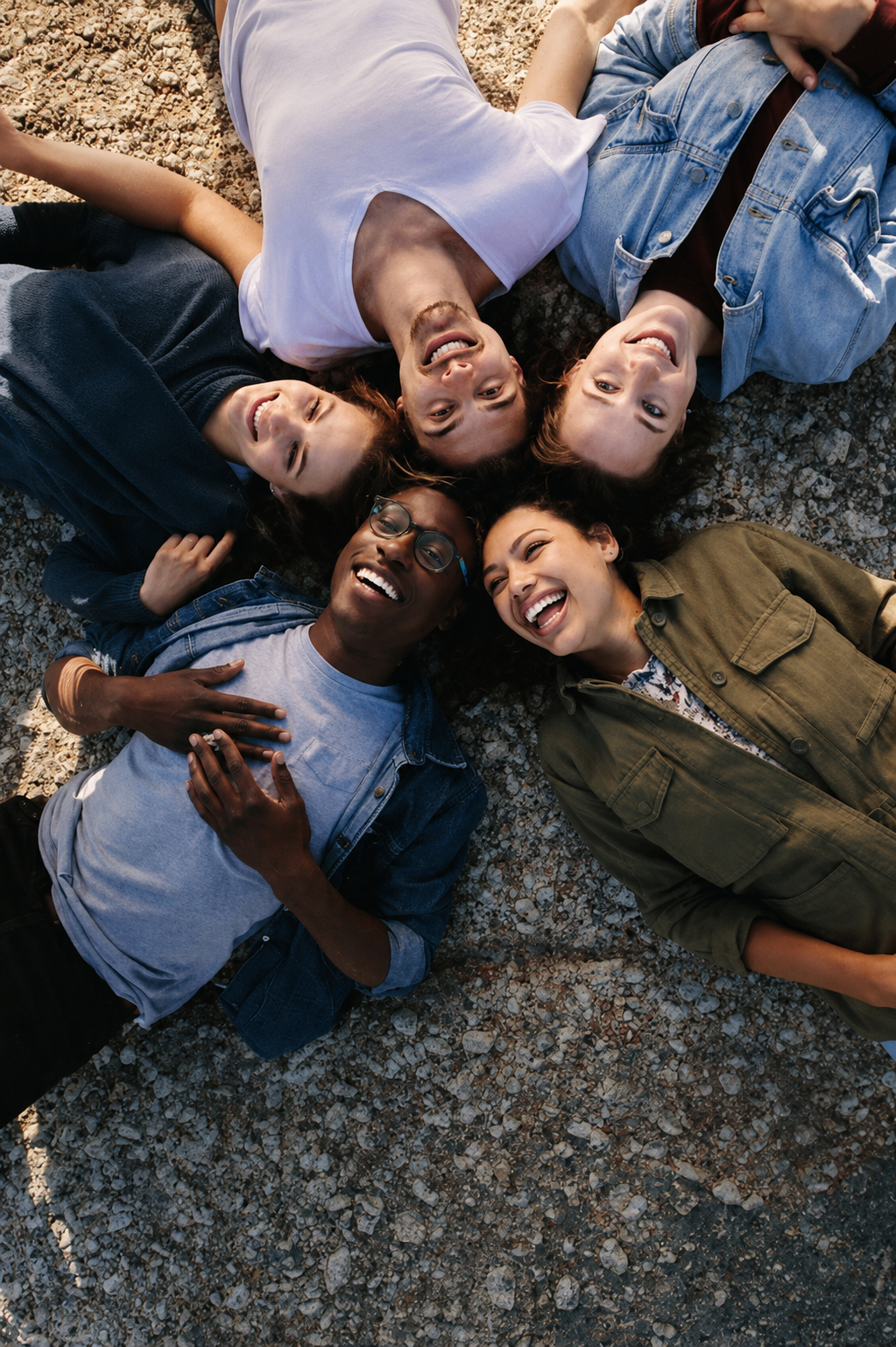 Five students lying in a circle on the ground, heads together, laughing