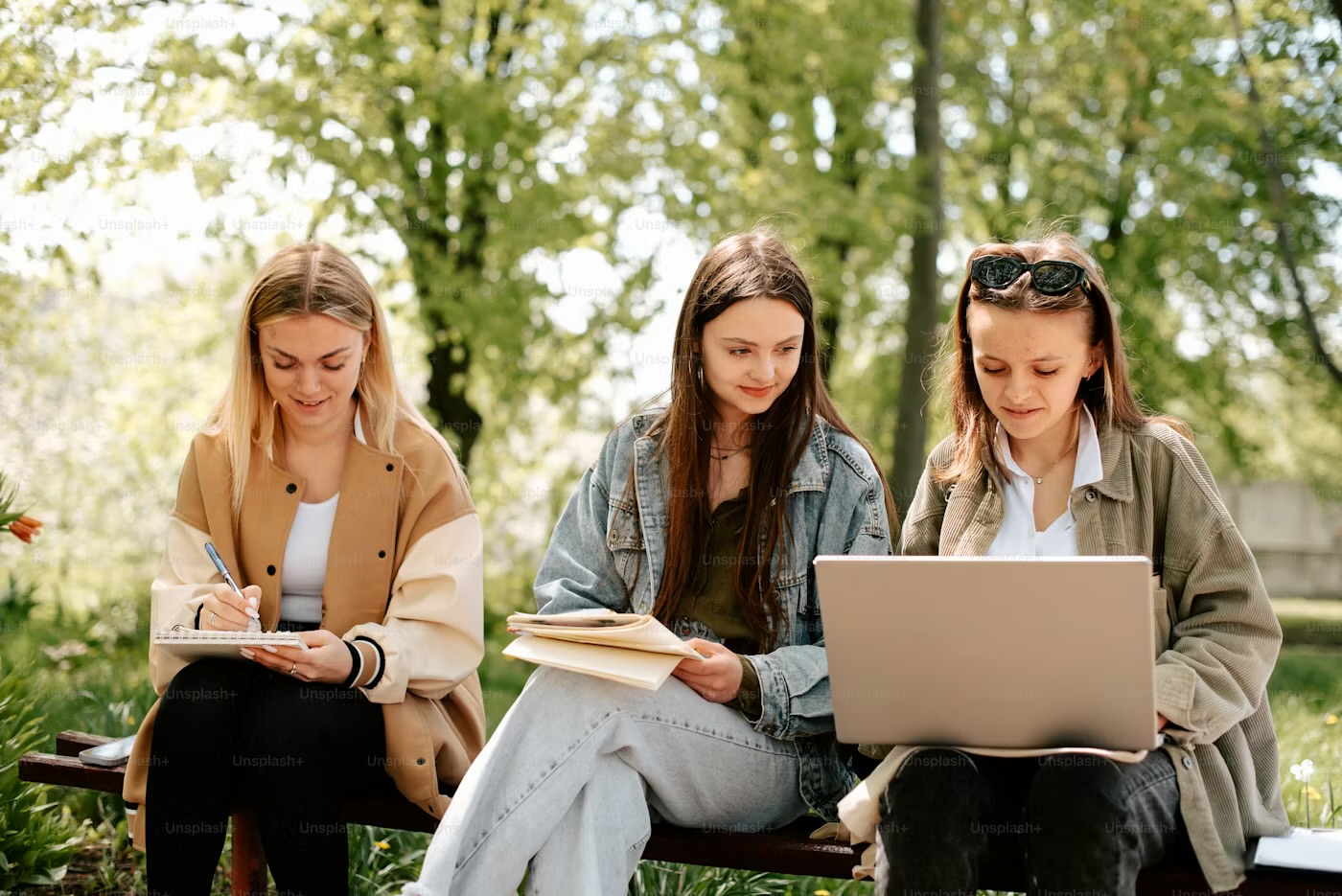 Three students studying on a park bench with a laptop